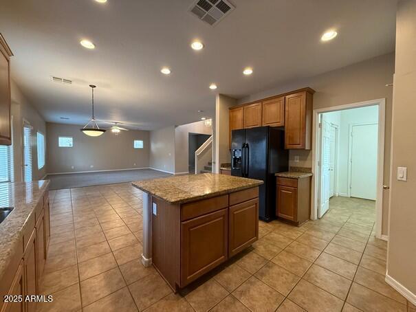 kitchen with light tile patterned floors, black refrigerator with ice dispenser, light stone countertops, and a kitchen island