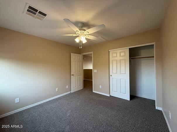 unfurnished bedroom with ceiling fan, a closet, and dark colored carpet