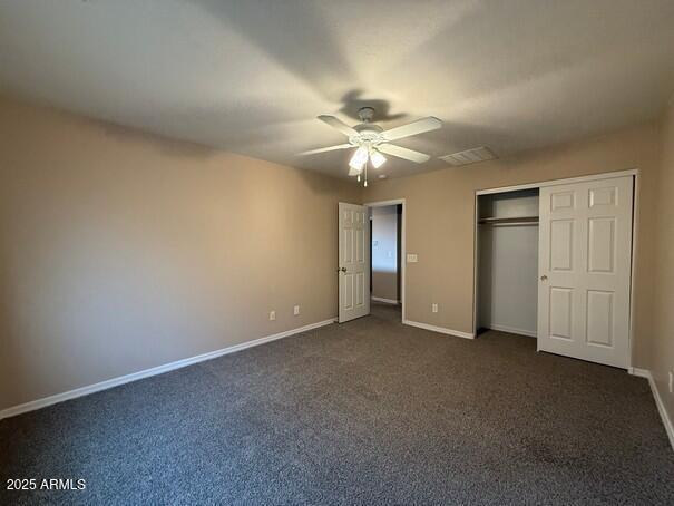 unfurnished bedroom with dark colored carpet, ceiling fan, and a closet