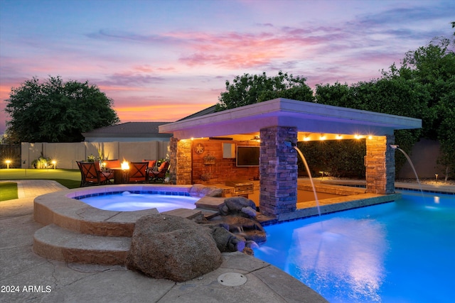 pool at dusk with pool water feature, a patio, and an in ground hot tub