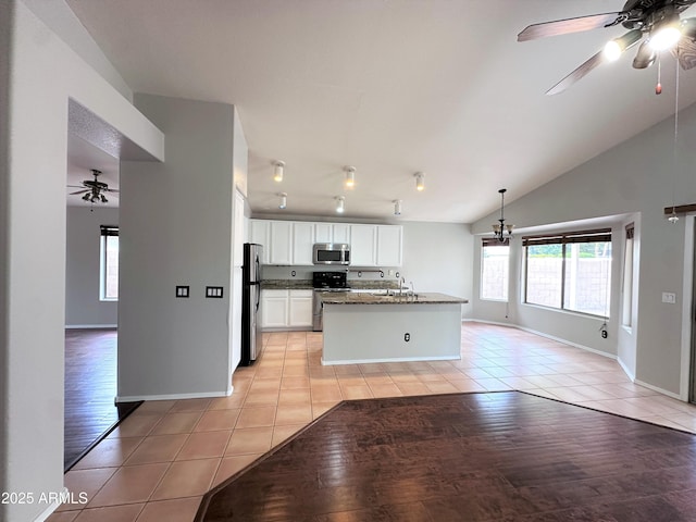 kitchen with light tile patterned floors, appliances with stainless steel finishes, an island with sink, white cabinets, and dark stone counters