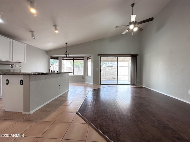 kitchen featuring vaulted ceiling, sink, light tile patterned floors, white cabinets, and ceiling fan with notable chandelier