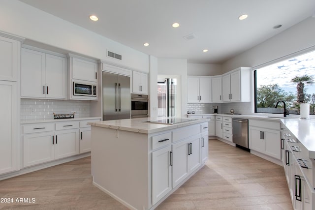 kitchen with white cabinets, built in appliances, a kitchen island, and light hardwood / wood-style floors