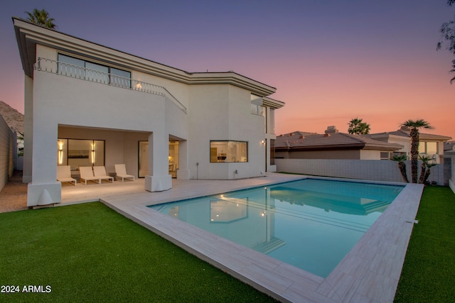 back house at dusk with a patio area, a fenced in pool, and a lawn