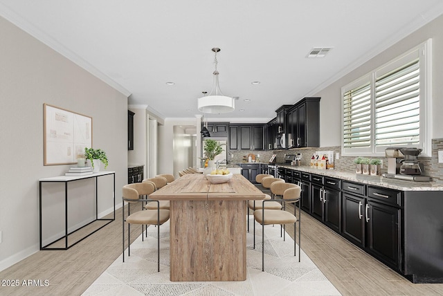 kitchen with visible vents, a breakfast bar, ornamental molding, dark cabinets, and backsplash