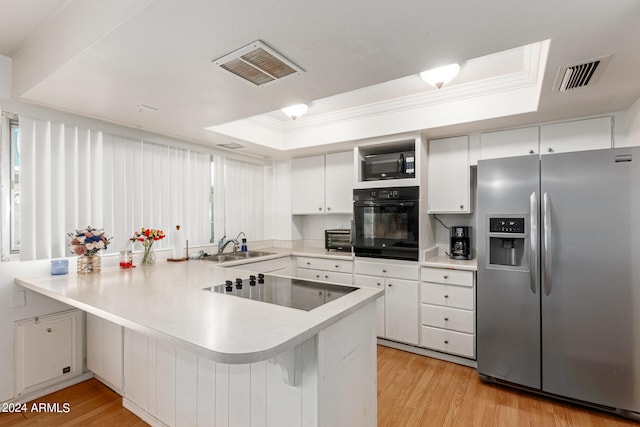 kitchen featuring light wood-type flooring, black appliances, a raised ceiling, and kitchen peninsula