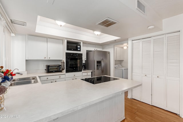 kitchen with a tray ceiling, black appliances, separate washer and dryer, and kitchen peninsula