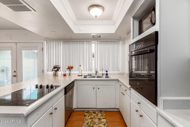 kitchen featuring a raised ceiling, black appliances, crown molding, sink, and light wood-type flooring