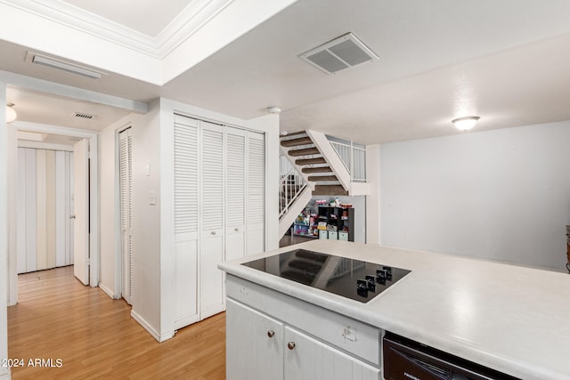 kitchen with black appliances, white cabinets, crown molding, and light hardwood / wood-style flooring