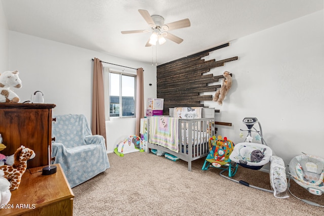 carpeted bedroom with ceiling fan and a crib