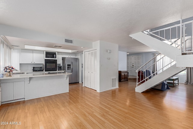 kitchen featuring black appliances, kitchen peninsula, light wood-type flooring, and white cabinets