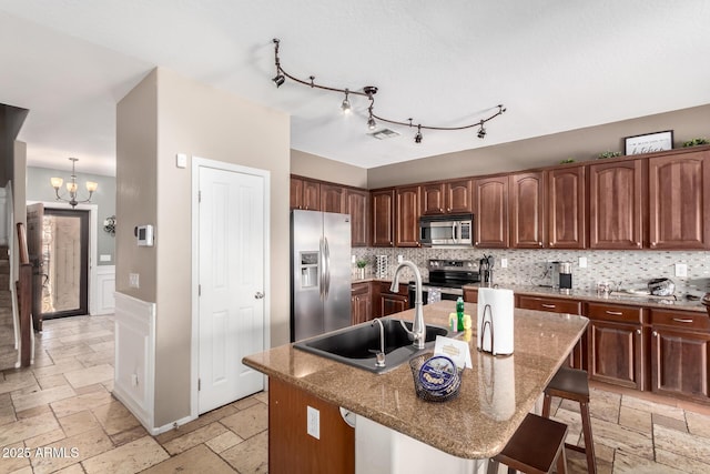 kitchen with sink, a breakfast bar area, stainless steel appliances, light stone countertops, and a center island with sink