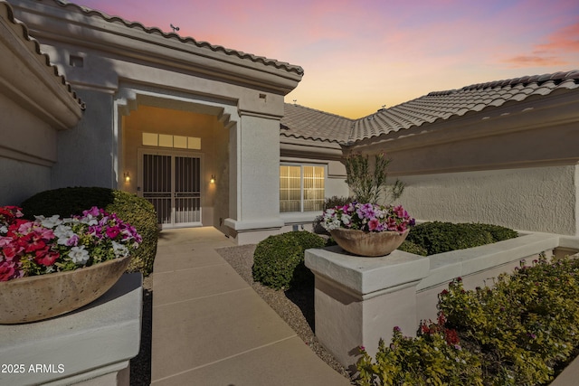 exterior entry at dusk featuring a tiled roof and stucco siding