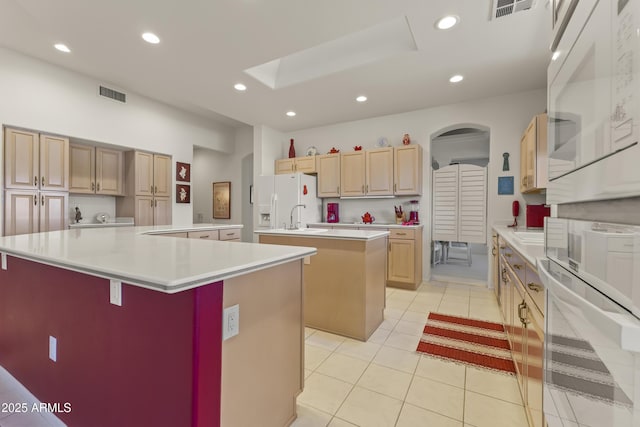 kitchen featuring white appliances, light brown cabinets, visible vents, and a large island with sink