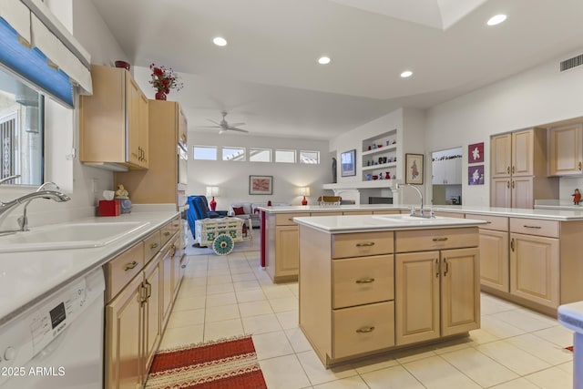 kitchen with light brown cabinets, white dishwasher, an island with sink, and a sink