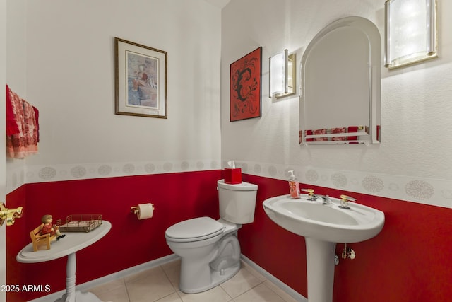 half bath featuring baseboards, a sink, toilet, and tile patterned floors