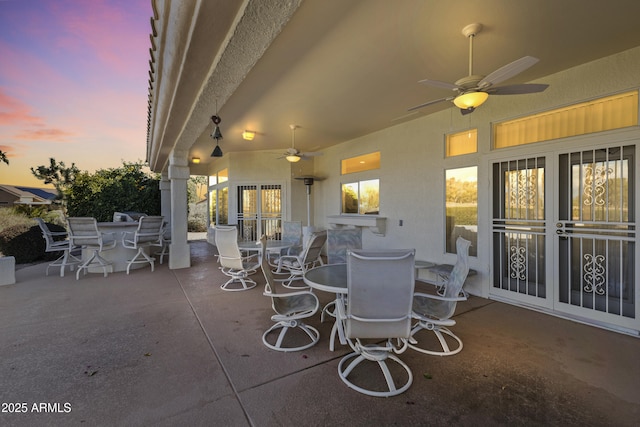 patio terrace at dusk featuring ceiling fan, french doors, and outdoor dining area