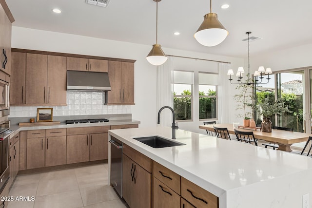 kitchen featuring sink, hanging light fixtures, a center island with sink, exhaust hood, and stainless steel gas stovetop