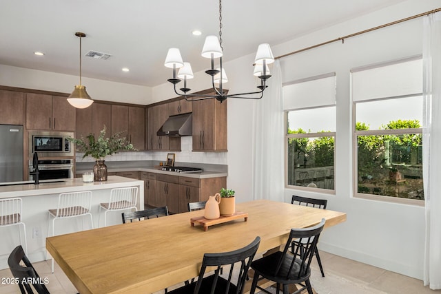 kitchen with appliances with stainless steel finishes, decorative light fixtures, tasteful backsplash, a kitchen breakfast bar, and dark brown cabinets