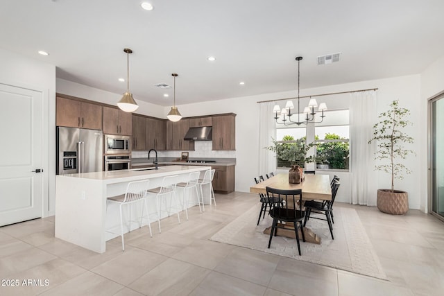 kitchen with sink, appliances with stainless steel finishes, dark brown cabinetry, tasteful backsplash, and an island with sink