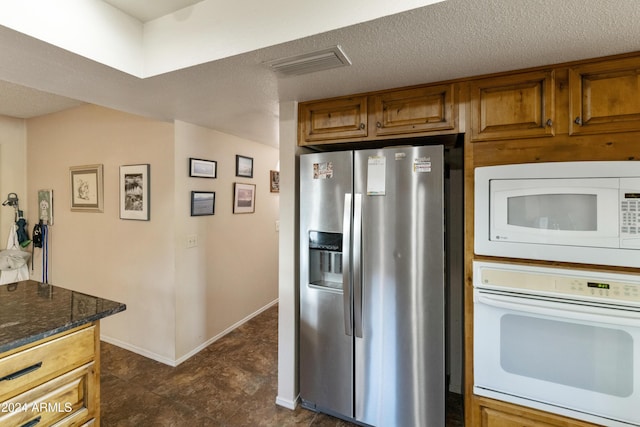 kitchen with white appliances, a textured ceiling, and dark stone counters