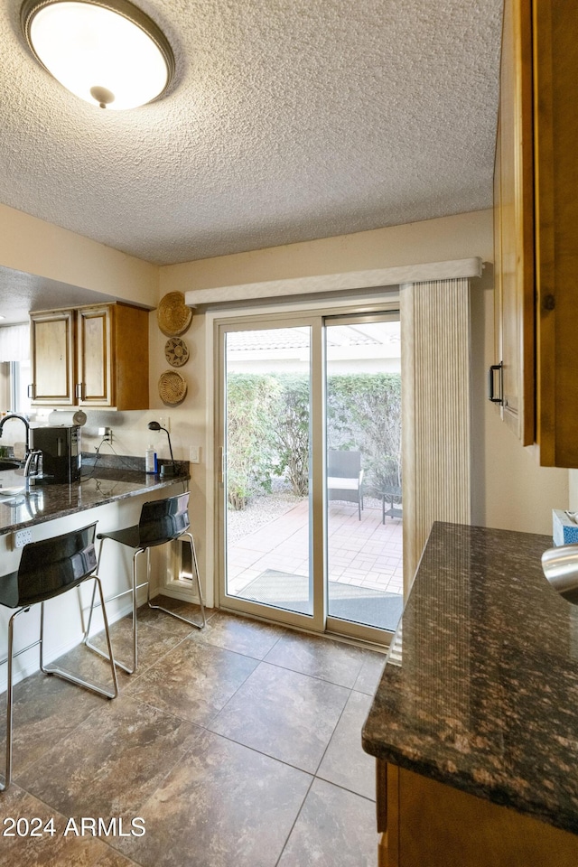 kitchen featuring sink, dark stone countertops, light tile patterned floors, and a textured ceiling