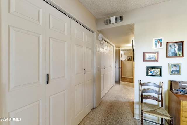 corridor featuring a textured ceiling and light colored carpet