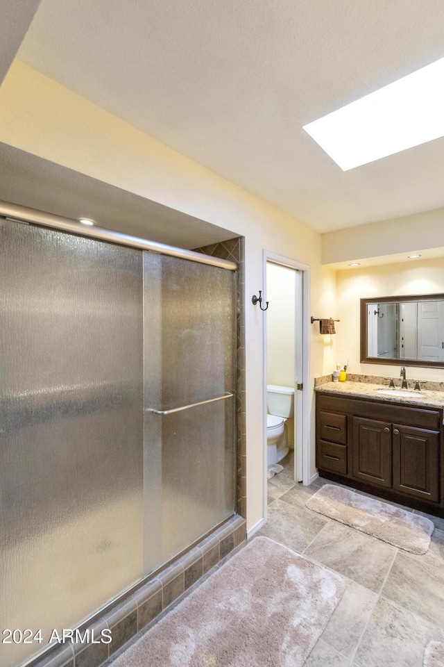 bathroom with a skylight, a shower with door, vanity, and toilet