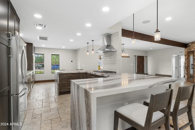 kitchen with beam ceiling, wall chimney range hood, light stone counters, stainless steel appliances, and hanging light fixtures