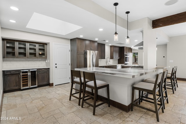 kitchen with appliances with stainless steel finishes, a kitchen breakfast bar, a skylight, light tile patterned flooring, and beverage cooler