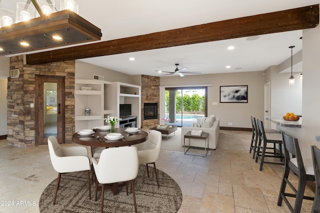 tiled dining space with beam ceiling, a stone fireplace, built in features, and ceiling fan