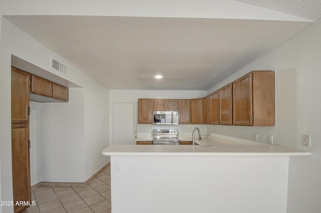 kitchen with light tile patterned flooring, appliances with stainless steel finishes, sink, kitchen peninsula, and a textured ceiling