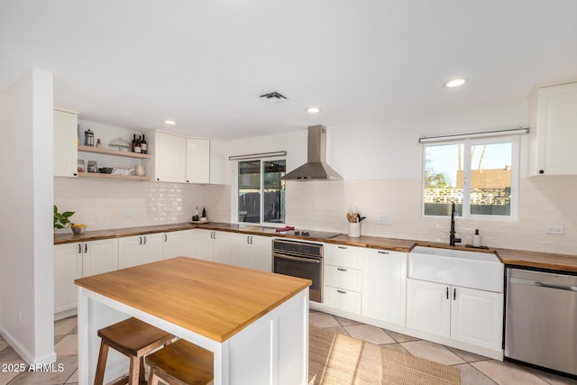 kitchen featuring light tile patterned flooring, stainless steel appliances, wood counters, white cabinetry, and wall chimney range hood