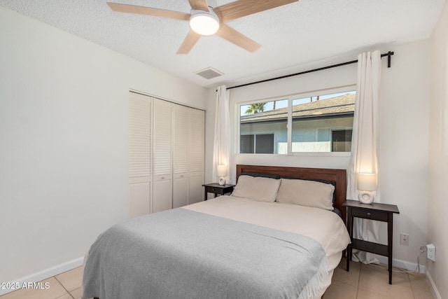 bedroom featuring baseboards, visible vents, light tile patterned flooring, a closet, and a textured ceiling