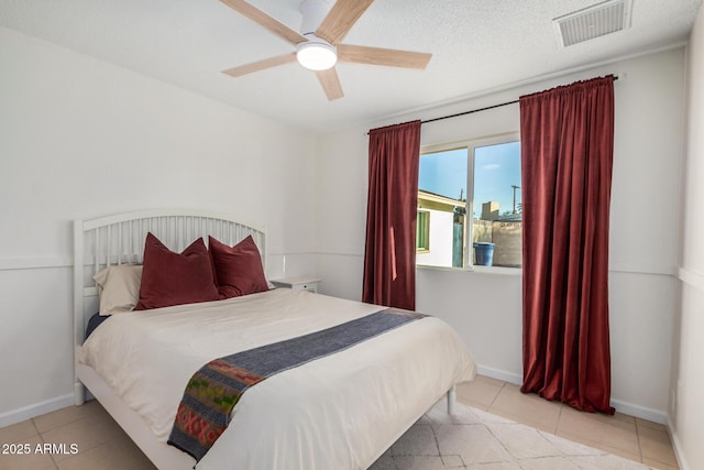 bedroom with a ceiling fan, baseboards, visible vents, tile patterned flooring, and a textured ceiling