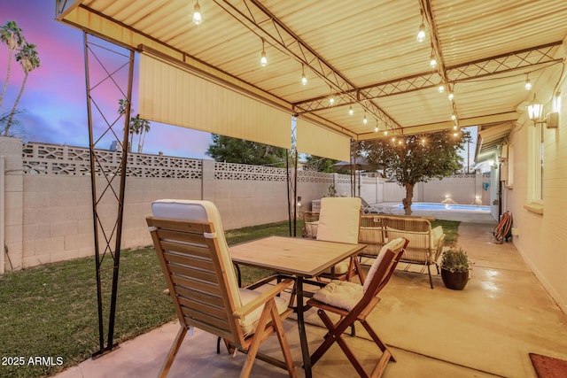 patio terrace at dusk featuring a swimming pool, outdoor dining area, and a fenced backyard