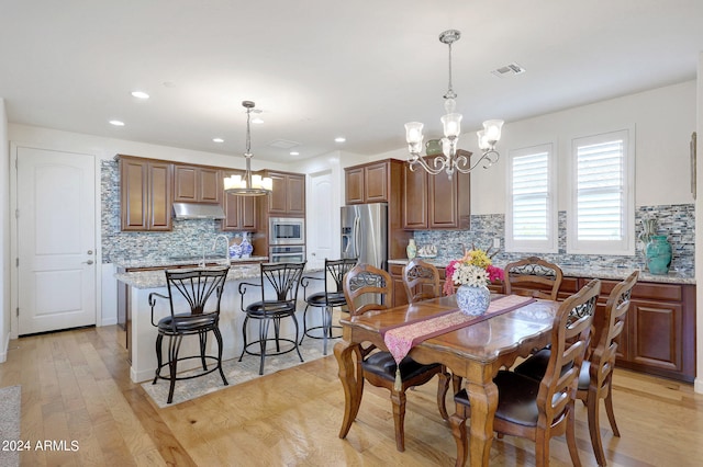 dining space with an inviting chandelier, sink, and light hardwood / wood-style floors