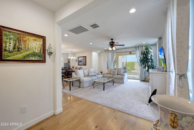 living room with ceiling fan with notable chandelier and light hardwood / wood-style floors