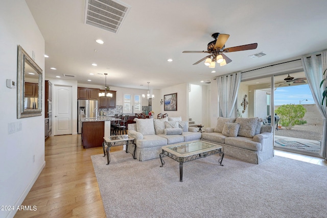 living room featuring light wood-type flooring, ceiling fan with notable chandelier, and plenty of natural light