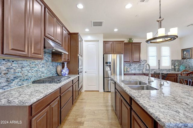 kitchen with appliances with stainless steel finishes, backsplash, pendant lighting, light hardwood / wood-style flooring, and sink