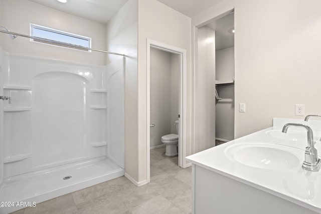 full bathroom with double vanity, baseboards, toilet, a shower stall, and a sink