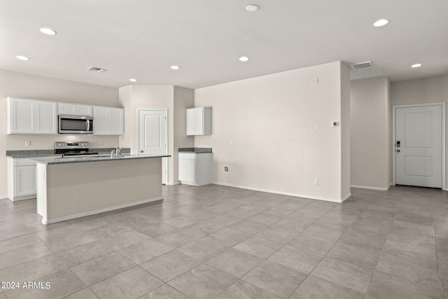 kitchen featuring appliances with stainless steel finishes, white cabinets, a center island with sink, and visible vents