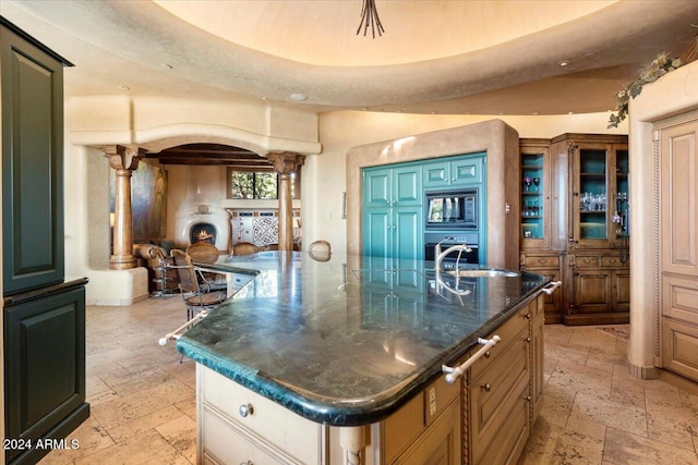 kitchen with oven, a large island with sink, built in microwave, ornate columns, and sink