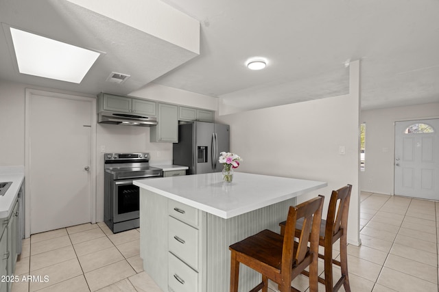 kitchen featuring light tile patterned floors, gray cabinetry, a kitchen island, stainless steel appliances, and a kitchen bar