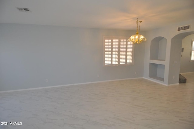 empty room featuring built in features and a notable chandelier