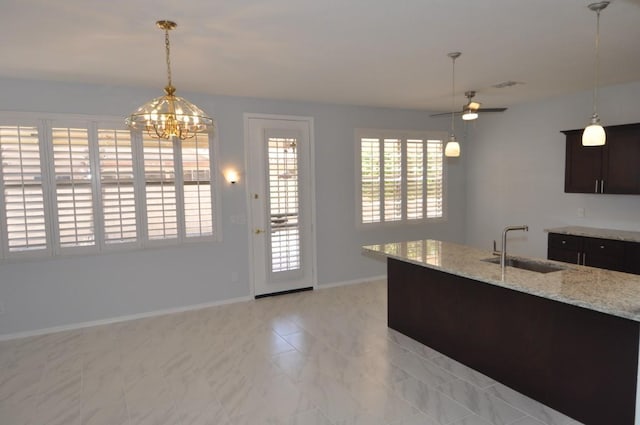 kitchen featuring light stone counters, decorative light fixtures, dark brown cabinetry, sink, and ceiling fan with notable chandelier