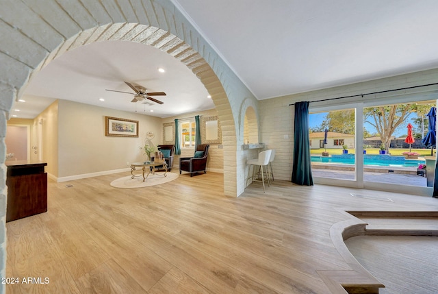 living room with light hardwood / wood-style floors, ceiling fan, and brick wall