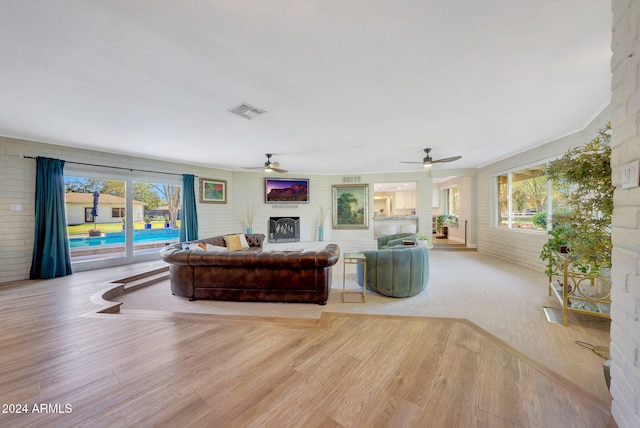 living room with ceiling fan, light hardwood / wood-style floors, and brick wall