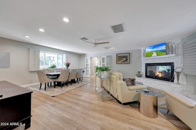 living room with light wood-type flooring, ceiling fan, and a fireplace