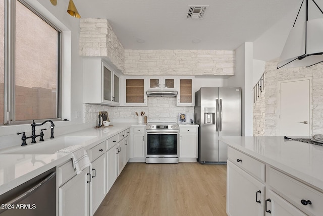 kitchen featuring light stone countertops, light wood-type flooring, stainless steel appliances, sink, and white cabinets